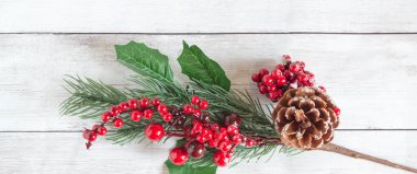 Kırmızı böğürtlenli ladin dallarından ve açık ahşap zemin üzerinde kahverengi çam kozalaklarından yapılmış Noel süslemeleri. Metin için alan, üst görünüm, düz alan. En alttan dal