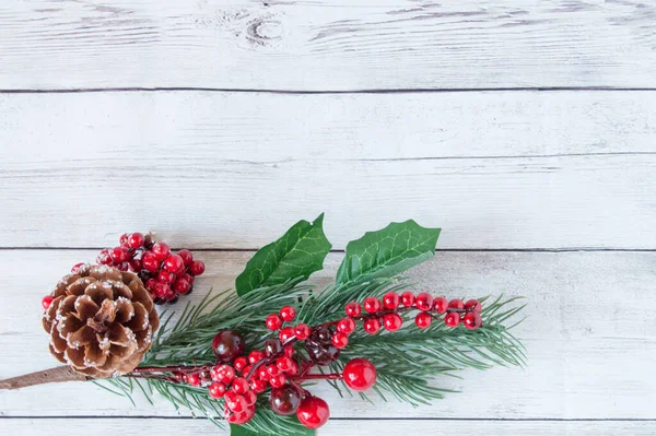 Juldekorationer av gran grenar med röda bär och bruna naturliga kottar furu på en ljus trä bakgrund. Utrymme för text, ovanifrån, platt ligg. Filial underifrån Stockfoto