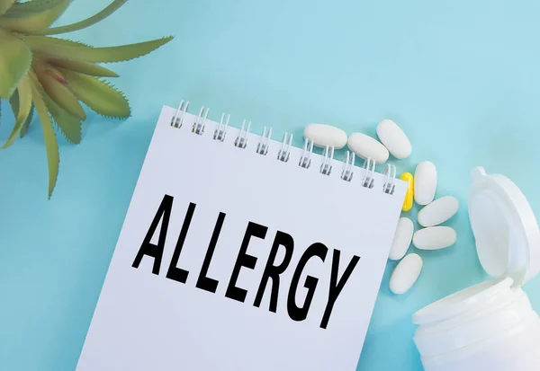A palavra Alergia em um papel Bloco de notas, pílulas e uma planta em um fundo azul, conceito médico de Alergia — Fotografia de Stock