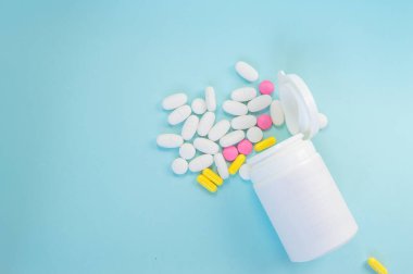 Mavi arka planda dağınık haplar bulunan plastik bir kavanoza yakın plan. İlaç ve eczane kavramı.