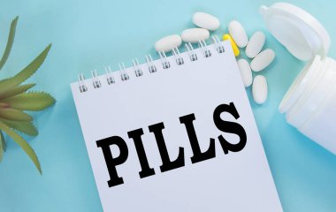 Mavi arka planda, ilaç, ilaç, ilaç ve sağlık konseptinin yanında duran beyaz bir not defterine yazılan haplar.