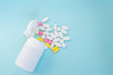 Mavi arka planda dağınık haplar bulunan plastik bir kavanoza yakın plan. İlaç ve eczane kavramı.