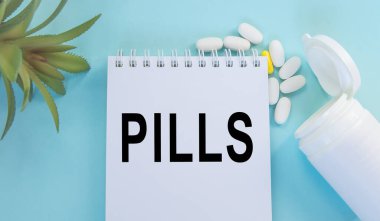 Mavi arka planda, ilaç, ilaç, ilaç ve sağlık konseptinin yanında duran beyaz bir not defterine yazılan haplar.