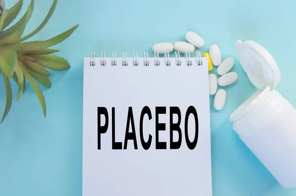 A palavra placebo escrito em um bloco de notas, ao lado de comprimidos e uma flor no fundo — Fotografia de Stock