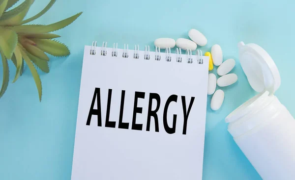 A palavra Alergia em um papel Bloco de notas, pílulas e uma planta em um fundo azul, conceito médico de Alergia — Fotografia de Stock