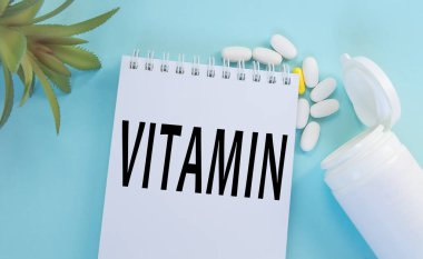 Mavi arkaplan tabletleri ve VITAMIN tıp ve PHARMACY kavramının yazılı olduğu Notepad üzerindeki en üst görünüm