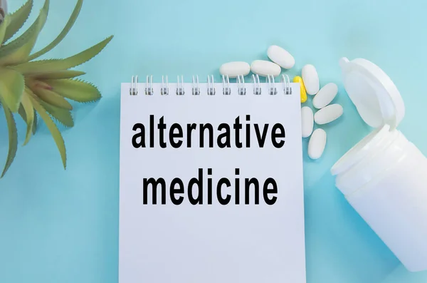 Medicina alternativa-escrita em um bloco de notas deitado sobre a mesa entre as pílulas e a flor, a escolha de métodos de tratamento — Fotografia de Stock