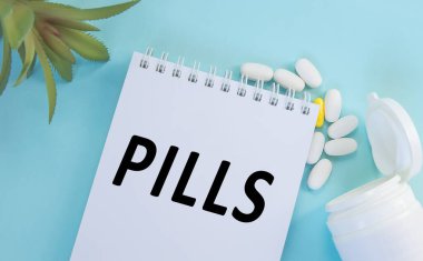 Mavi arka planda, ilaç, ilaç, ilaç ve sağlık konseptinin yanında duran beyaz bir not defterine yazılan haplar.