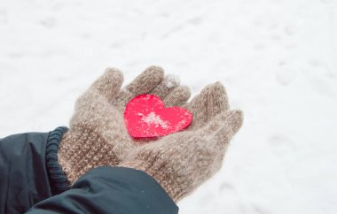 Sıcak yün eldiven ören kadınların elleri, kışın, Sevgililer Günü konsepti olan karın arka planında kırmızı bir kalbi tutar.