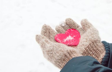 Sıcak yün eldiven ören kadınların elleri, kışın, Sevgililer Günü konsepti olan karın arka planında kırmızı bir kalbi tutar.
