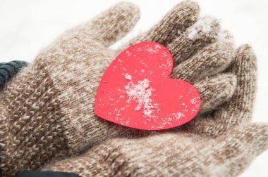 Sıcak yün eldiven ören kadınların elleri, kışın, sevgililer günü konsepti, yakın plan, karın arka planında kırmızı bir kalp tutar.