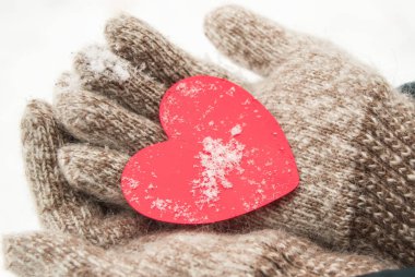 Sıcak yün eldiven ören kadınların elleri, kışın, sevgililer günü konsepti, yakın plan, karın arka planında kırmızı bir kalp tutar.