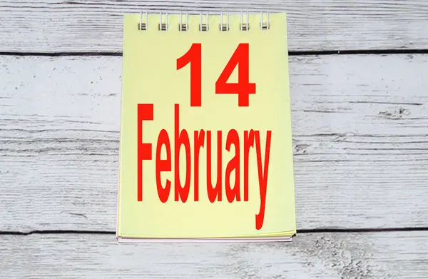 Glad Alla hjärtans dag koncept, gul anteckningsblock sida med text på februari 14 På ljus trä bakgrund — Stockfoto