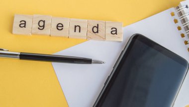 Masaüstündeki tahta küplere yazılmış plan. Kalem, telefon ve kağıt. Sarı arka plan, üst manzara, düz düzen.