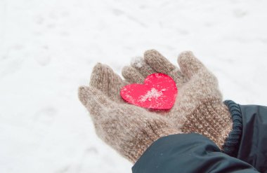 Sıcak yün eldiven ören kadınların elleri, kışın, Sevgililer Günü konsepti olan karın arka planında kırmızı bir kalbi tutar.