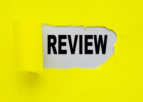 Yellow torn paper with a hole and the word REVIEW on a gray background, the concept OF ANALYSIS AND VERIFICATION — Stock Photo, Image