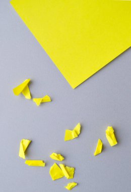 Köşedeki YELLOW kağıdında gri bir arkaplan üzerindeki boşluğun bir kopyası ve küçük yırtık ve buruşuk kağıt parçaları, tasarımınız için bir şablon, dikey