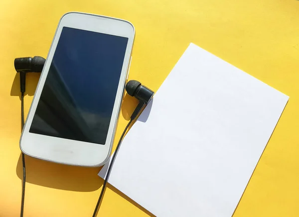 Modern sosyal uygulama klubünü akıllı telefon, kulaklık ve sarı arka planda boşluğun bir kopyası olan boş bir sayfada kullanma kavramı.