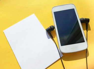 Modern sosyal uygulama klubünü akıllı telefon, kulaklık ve sarı arka planda boşluğun bir kopyası olan boş bir sayfada kullanma kavramı.