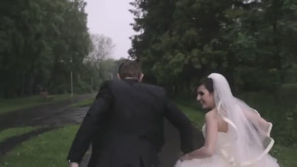 Bruid en bruidegom lopen onder de regen — Stockvideo