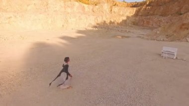 Güzel bir kadın sarı dağların arasında sarı kum boyunca yalınayak beyaz piyanoya doğru yürür. Hava görüntüsü. Sürrealizm.