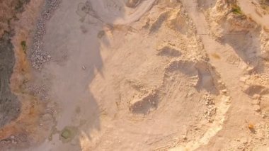 Devasa bir kum çukurunun dibindeki havadan görünüşü. Bir adam kumlu bir taş ocağında piyano çalıyor. Sürrealizm.