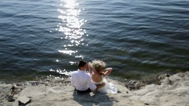 Los novios se sientan junto al río el día de su boda. Desenfoque — Vídeos de Stock