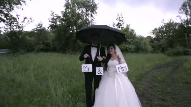 Весілля під дощем. Наречений і наречений під дощем тримають знаки пан і місіс . — стокове відео