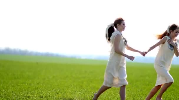 Két fehér ruhás ikerlány mezítláb rohangál zöld füvön a réten.. — Stock videók