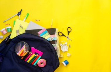 Sarı arka planda okul malzemeleriyle dolu bir sırt çantası. Yukarıdan bak. Kopyalama alanı, okul ücretleri konsepti