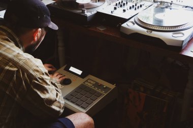 A hip hop composer, beatmaker creates beats on a digital production controller with pushbutton pads. The DJ plays the beats live on the pad controller of digital audio equipment. Rap music