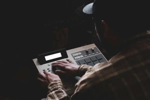 A hip hop composer, beatmaker creates beats on a digital production controller with pushbutton pads. The DJ plays the beats live on the pad controller of digital audio equipment. Rap music