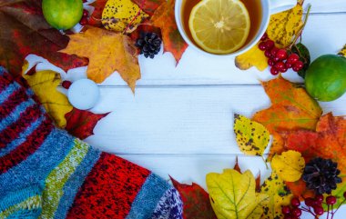 Sonbahar arkaplan ahşap masa sarı yapraklı ve sıcak çoraplı limonlu sıcak çay, fotokopi alanı, yumuşak odaklı