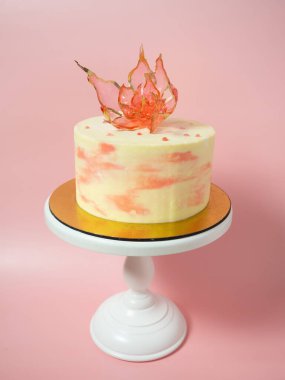 Pembe arka planda, izomalt kekin üstünde yenilebilir kırmızı bir çiçek.