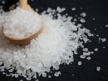 Deniz tuzu, ahşap bir kaşıkta eski ahşap bir arka planda deniz tuzu yığını.