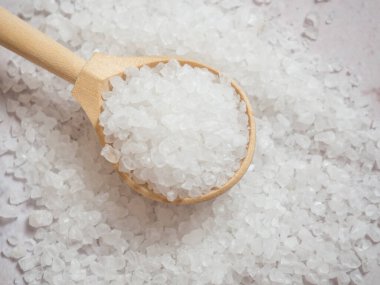 Deniz tuzu, ahşap kaşıkta hafif beton arka planda bir yığın deniz tuzu.