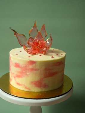 Pastanın üzerinde soluk yeşil bir arka planda, yenilebilir kırmızı bir izomalt çiçeği.