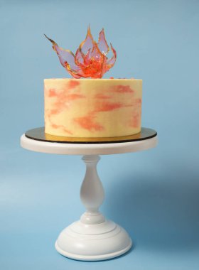 Mavi arkaplanda, pastanın üstünde yenilebilir kırmızı bir izomalt çiçeği.