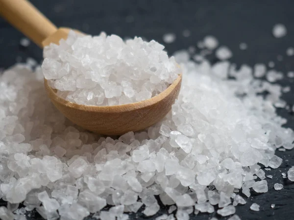 sea salt, a pile of sea salt in a wooden spoon on an old wooden background close-up