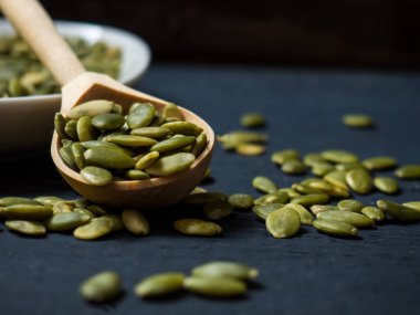 Beyaz kasede kabak çekirdeği ve tahta kaşık, yakın plan siyah ahşap arka plan. metin alanı kopyalanıyor