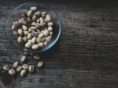 Eski ahşap bir masanın üzerinde temiz cam bir kasede fıstıklar atmosferik bir kırsal kompozisyon, bir kopya alanı.
