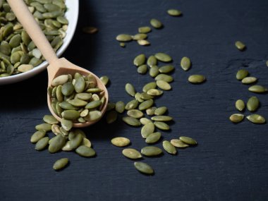 Beyaz kasede kabak çekirdeği ve tahta kaşık, yakın plan siyah ahşap arka plan. metin alanı kopyalanıyor