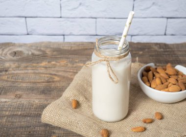 bir şişe badem sütü ve sade ahşap arka planda badem ezmesi.