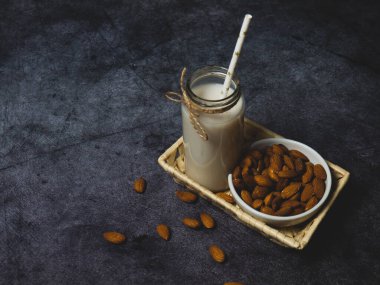 Şişedeki badem sütü ve tahta kasedeki bademler, metin için arka plandaki siyah taş kopyalama alanı.