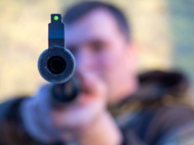 Bir adam objektife nişan alıyor, havalı tüfeğin namlusuna yakın plan.