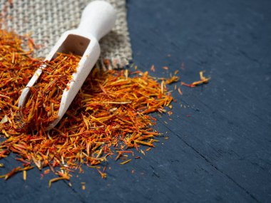 Siyah arka planda, tahta kaşıkta kurumuş safran baharatları.