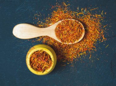 Siyah arka planda, tahta kaşıkta kurumuş safran baharatları.