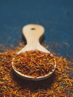 Siyah arka planda, tahta kaşıkta kurumuş safran baharatları.