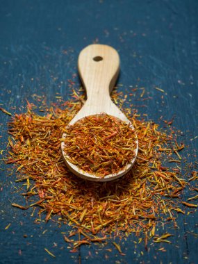 Siyah arka planda, tahta kaşıkta kurumuş safran baharatları.