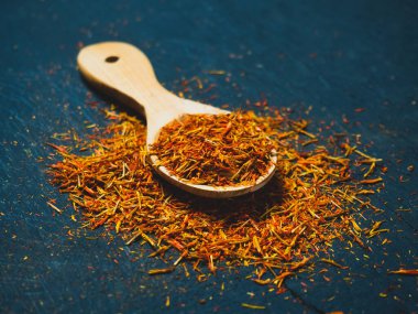 Siyah arka planda, tahta kaşıkta kurumuş safran baharatları.